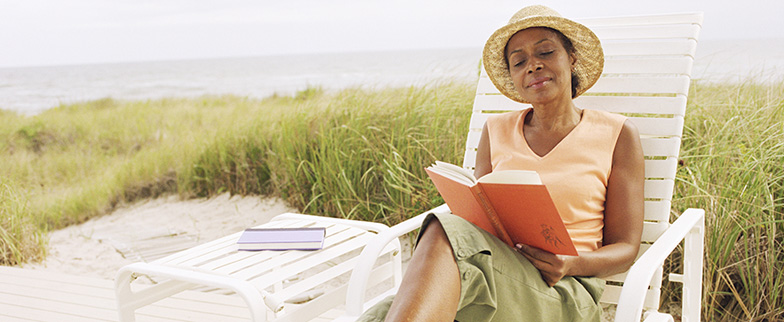 Woman outside with hat on reading a book.