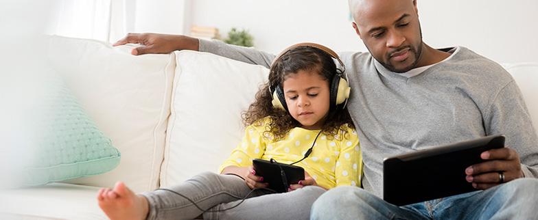 Child and parent on couch with electronic devices.
