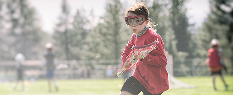 Child playing lacrosse with special glasses on.